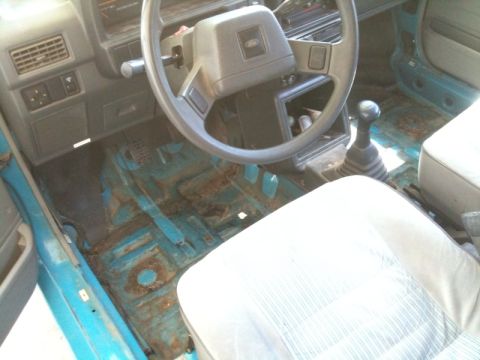 1991 Ford Festiva - Interior view of a 1991 Ford Festiva, highlighting the manual transmission and rusted floor panels.