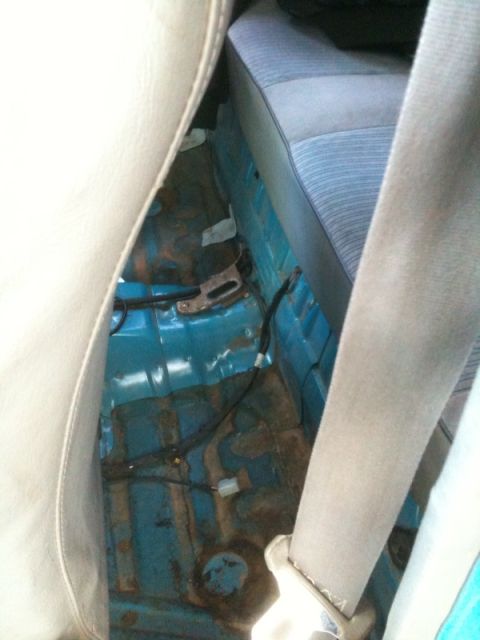 1991 Ford Festiva - The interior floor of a vehicle is exposed, showing dirt and wiring beneath the rear seat.