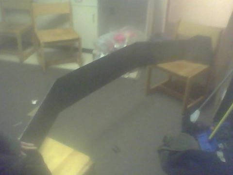 2000 Dodge 1500 - Unidentified black curved object, likely a car part, is shown in a room with chairs and cabinets.