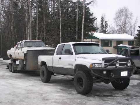 1990 Chevrolet Suburban - A white pickup truck tows another white pickup truck on a trailer in a snowy environment.