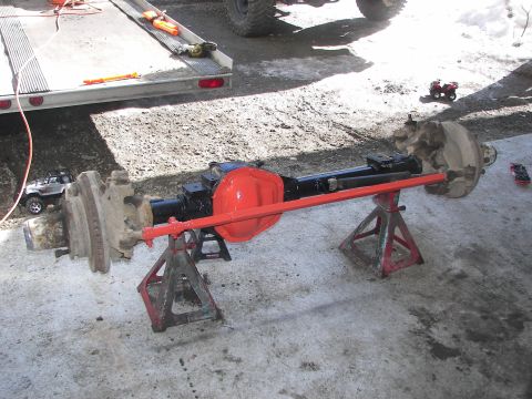 1990 Chevrolet Suburban - Front axle assembly, likely from a truck or SUV, is supported by jack stands with a red differential cover.