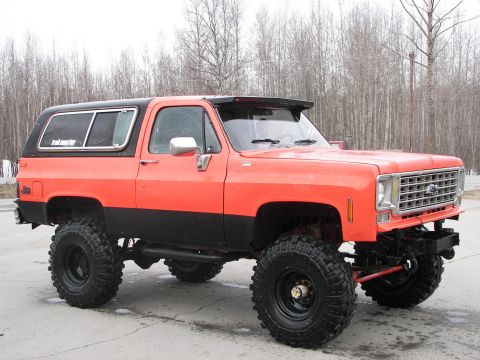 1990 Chevrolet Suburban - This lifted SUV features a two-tone orange and black paint scheme and aggressive off-road tires, with a grille indicative of a 1973 model.