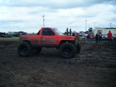 2000 Dodge 1500 - A modified orange pickup truck sits in a muddy area with people and other vehicles in the background.