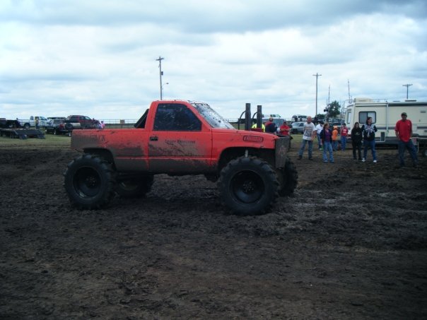 Orange pickup truck with large tires in mud, side view