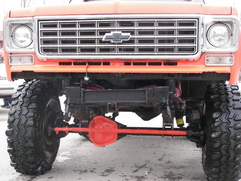 1990 Chevrolet Suburban - Close-up of the front grille and suspension of an orange pickup truck, large off-road tires.
