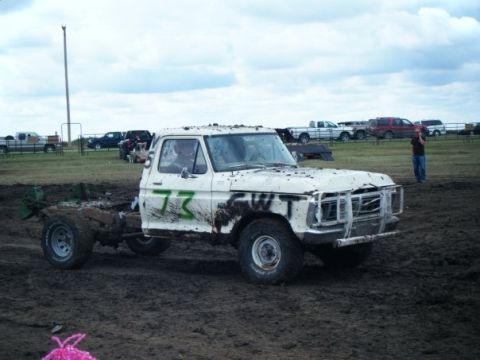 2000 Dodge 1500 - A mud-covered white pickup truck with racing numbers is seen in a muddy field, possibly at a mud bog event.