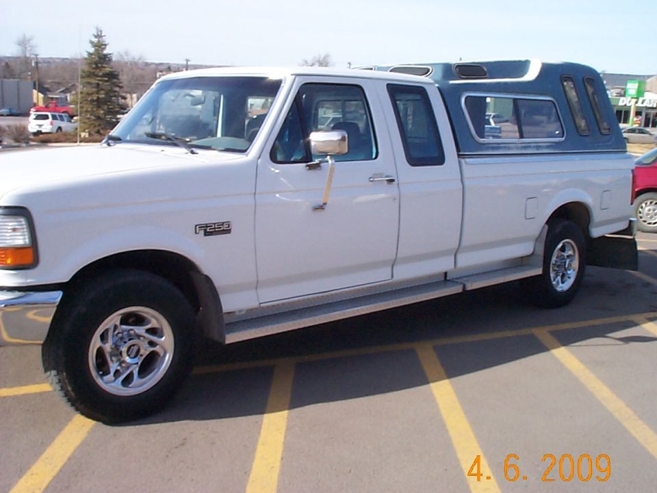 White 1995 Ford F-250 pickup truck with a blue camper shell, seen from the side