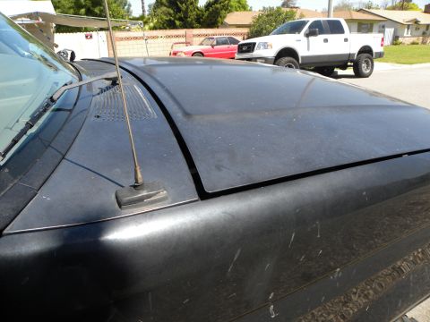 1995 Ford Bronco - Close-up of a black SUV's hood and windshield area, with a white pickup truck visible in the background.