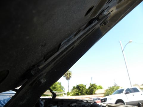 1995 Ford Bronco - The underside of a car hood is open, revealing the engine bay and a white truck parked nearby.