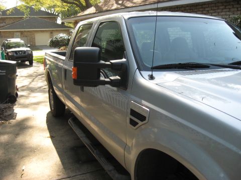 2008 Ford F-250 - A silver pickup truck is parked in a driveway next to a trash bin, with a dark SUV in the background.