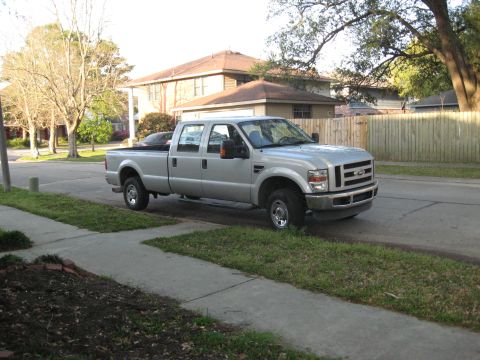 2008 Ford F-250 - A silver Ford F-250 Super Duty pickup truck is parked on the side of a street in front of a house and a wooden fence.