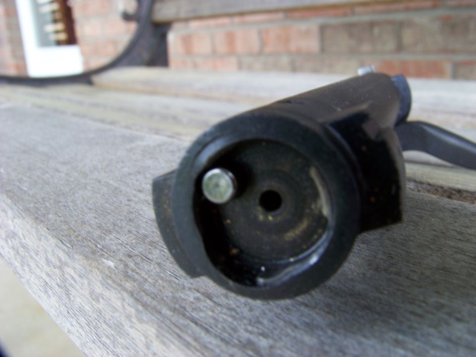 Close-up of a black tool part with a silver pin and a central hole, resting on a wooden surface