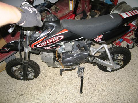 1986 Ford Bronco - This SDG Super Mini dirt bike is shown from the side, with a hand on the handlebars. The bike is parked indoors.