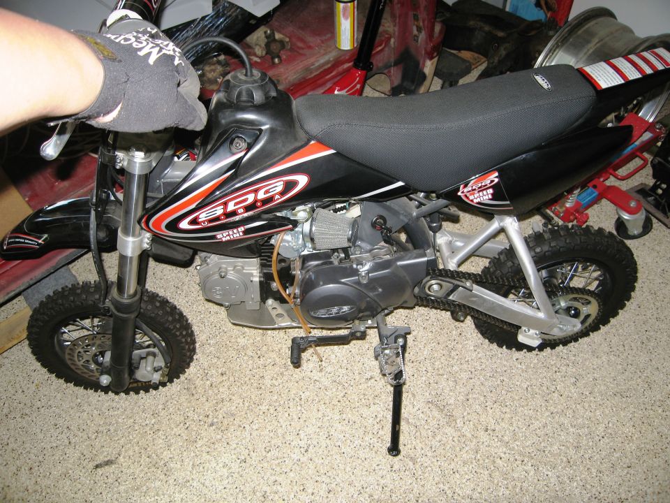 Dirt bike with SDG graphics and "Super Mini" text on the side. A hand in a black glove is on the handlebars