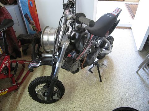 1986 Ford Bronco - A black dirt bike is parked indoors next to a red bicycle frame.
