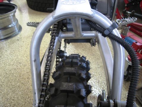 1986 Ford Bronco - Close-up of a motorcycle's rear frame, chain, and tire, with "SUPERMOTORS" visible on a watermark.