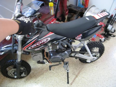 1986 Ford Bronco - A small dirt bike is parked indoors, with a hand on the handlebars and a "SUPERMOTORS" watermark at the bottom right.