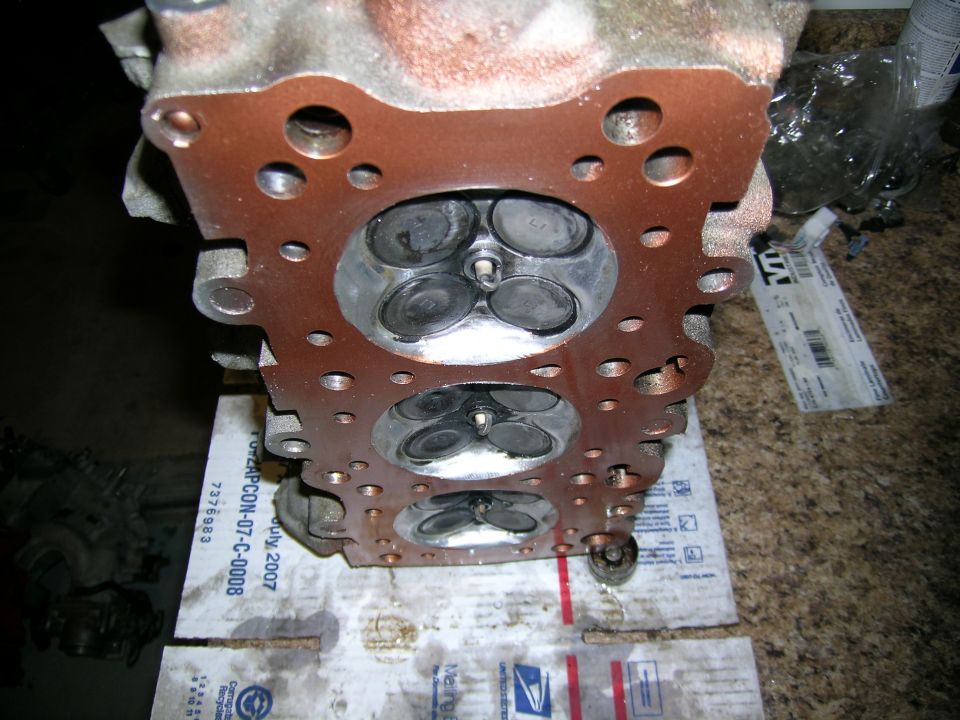 Engine cylinder head with valves visible, resting on cardboard