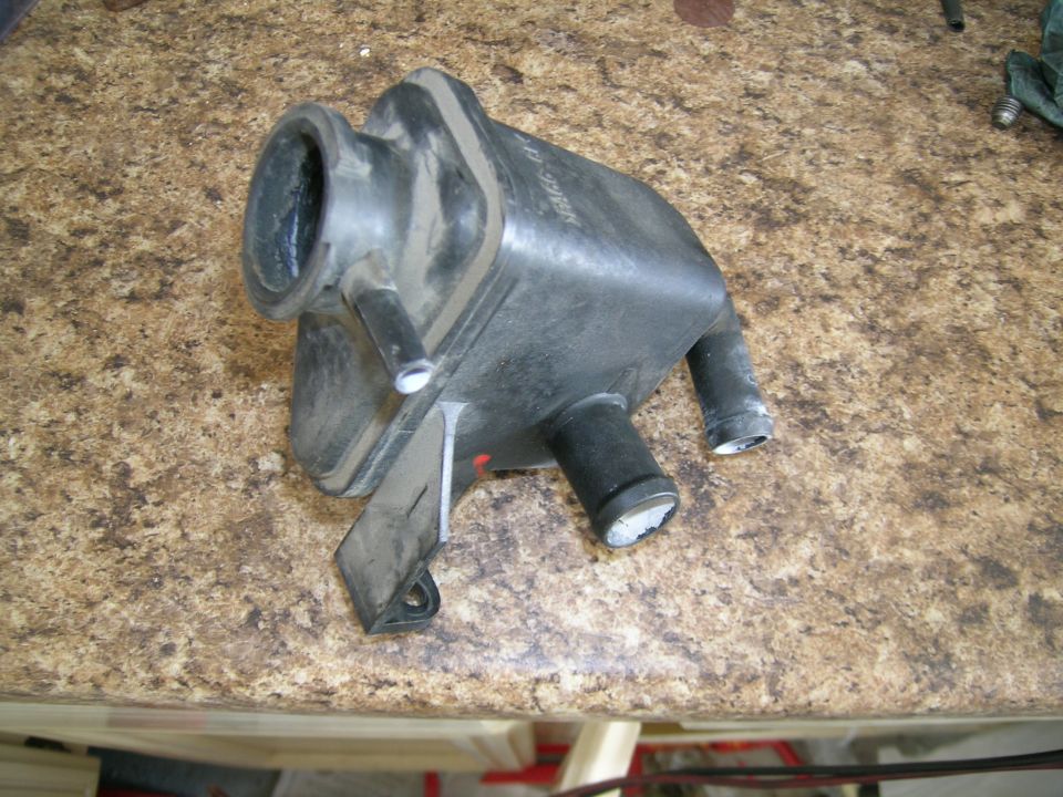 Plastic coolant reservoir with two hose connections and a mounting bracket. Text is visible on the side