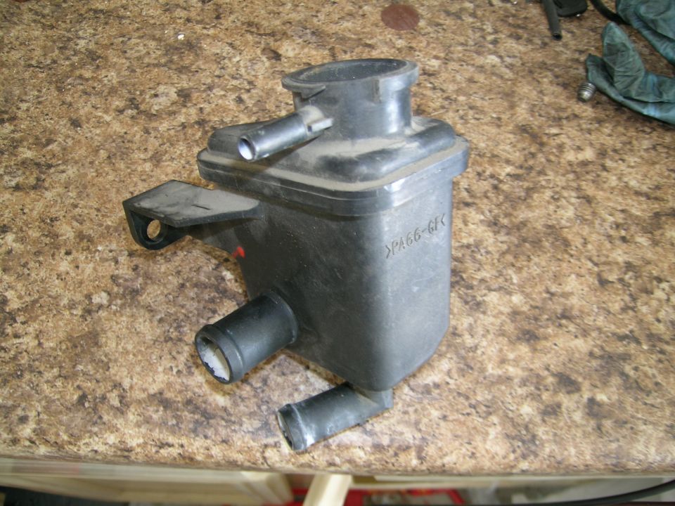 Black plastic power steering fluid reservoir with hoses attached. Text on side reads >PA66-GF<