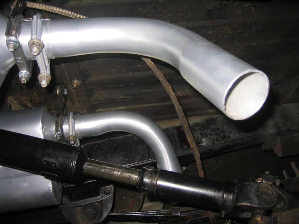 Silver exhaust pipe with turned-down tip near a driveshaft