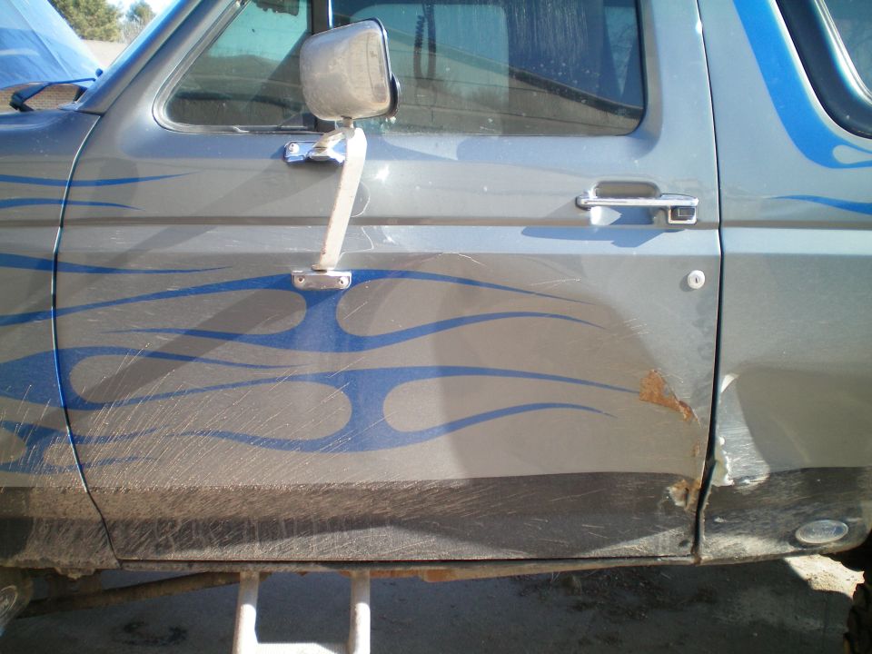Gray Ford Bronco side door with blue flame decals and rust spot