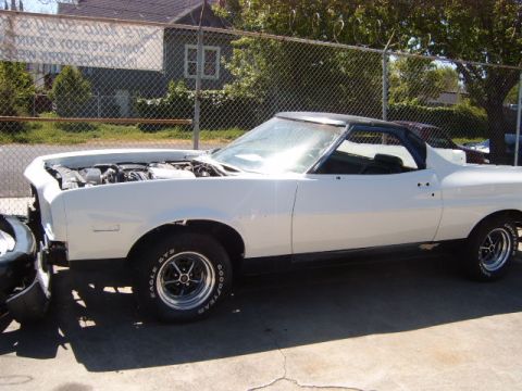 1973 Ford Ranchero - A white coupe utility with its hood open is parked outside next to a chain-link fence.