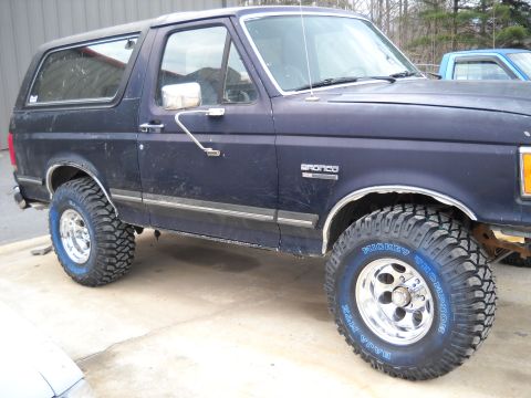 1982 Ford Bronco - A dark blue Ford Bronco is parked outdoors, showing its side profile and large off-road tires.
