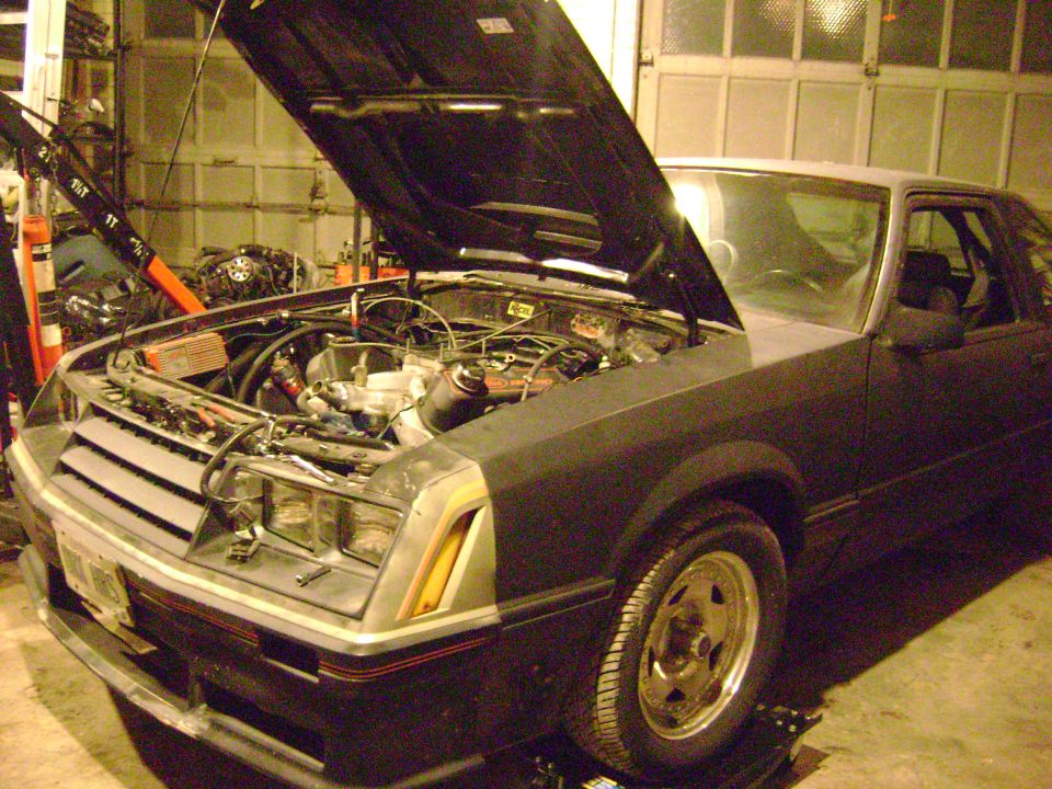 Dark gray 1981 Ford Mustang coupe with hood open, showing engine bay and front grille