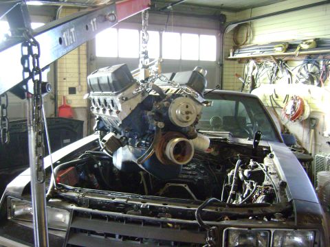 1981 Ford Mustang - Engine hoist lowering a V8 engine into a car's engine bay.