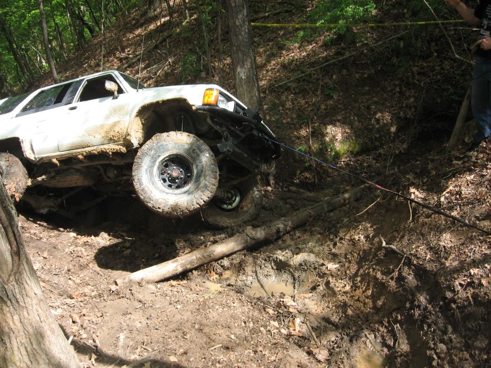 White off-road SUV stuck in mud, front wheel lifted