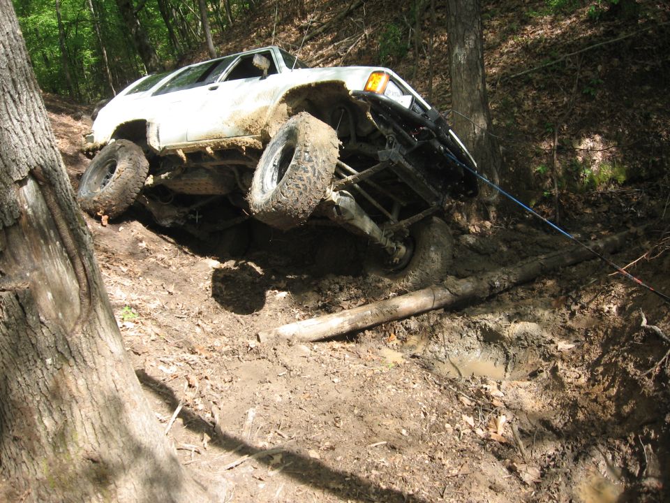 1984 Ford Bronco II stuck in mud on a steep, wooded incline with a tow rope attached