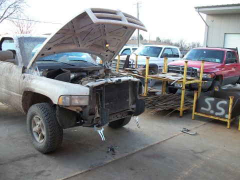 2000 Dodge 1500 - White Dodge Ram pickup truck with hood open and front end disassembled, parked outside near other trucks.