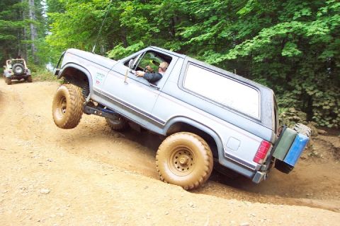 2002 Ford F-350 - A lifted Ford Bronco navigates an off-road trail, with a Jeep following in the background.