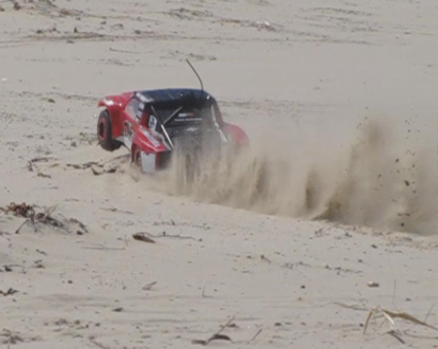 Red remote control trophy truck kicking up sand on a beach