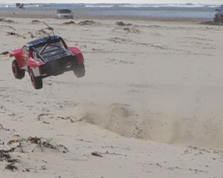 Red remote control truck mid-air on a sandy beach