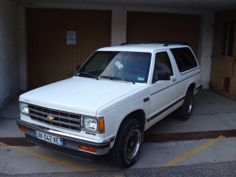 1991 Ford Crown Victoria - White 1983 Chevrolet S-10 Blazer with a blue stripe detail parked in front of garage doors.