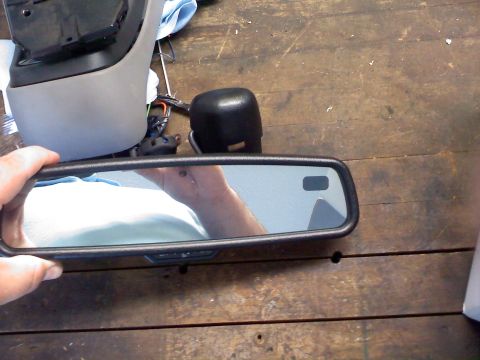 1992 Ford Bronco - A person is holding a vehicle's interior rear-view mirror assembly, with other car parts scattered on a wooden workbench.