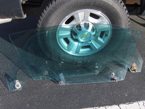 1980 Chevrolet Camaro - A car door window glass is placed on the ground in front of a vehicle's tire.