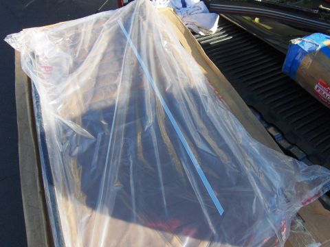 1980 Chevrolet Camaro - A car part, possibly a window or panel, is protected by plastic wrap and cardboard while being transported in a truck bed.