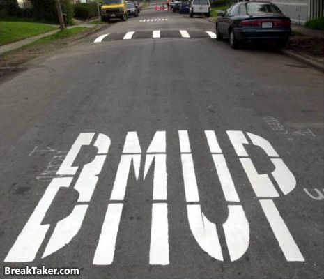 1989 Ford Bronco - White letters painted on asphalt with speed bumps. Multiple vehicles are visible on the street.