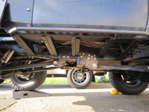 1996 Ford Bronco - The undercarriage and suspension components of a dark SUV are visible, with another vehicle partially seen behind it.
