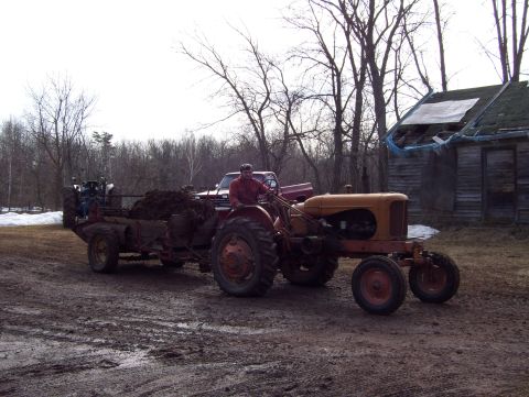 2000 Chevrolet Tahoe - A tractor tows a loaded trailer through a muddy yard, with a pickup truck parked nearby.