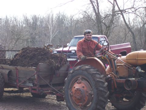 2000 Chevrolet Tahoe - Man driving a tractor that is pulling a manure spreader, with a red pickup truck in the background.