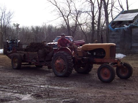 2000 Chevrolet Tahoe - A man drives an old tractor pulling a loaded trailer through a muddy field.