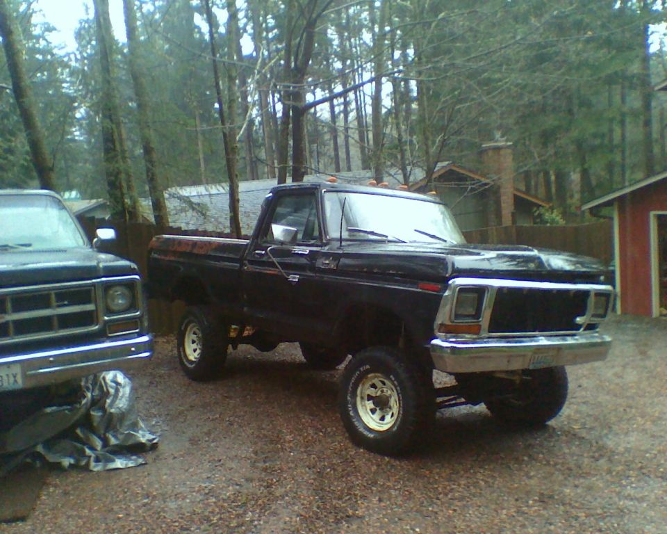 Black Ford F-Series truck with lifted suspension and chrome bumper, parked next to another truck