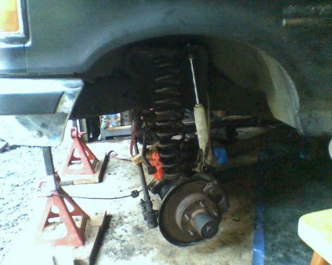1987 Ford Bronco - The front suspension and brake assembly of a 1987 Ford Bronco is visible while supported by jack stands.
