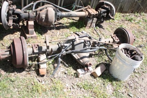 1990 Ford F-150 - Two disassembled vehicle rear axles are displayed outdoors, resting on brick supports with a bucket of parts beside them.