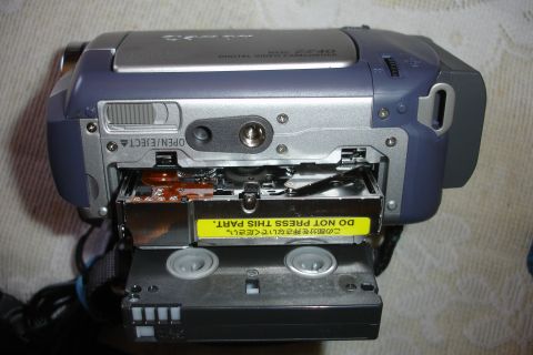 1993 Ford Taurus - A digital video camcorder is shown with its tape loading mechanism exposed, a yellow warning label in Japanese and English.