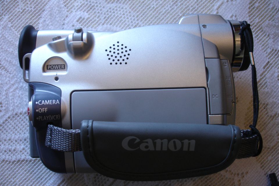 Silver Canon camcorder with a black hand strap, showing power button and mode selector